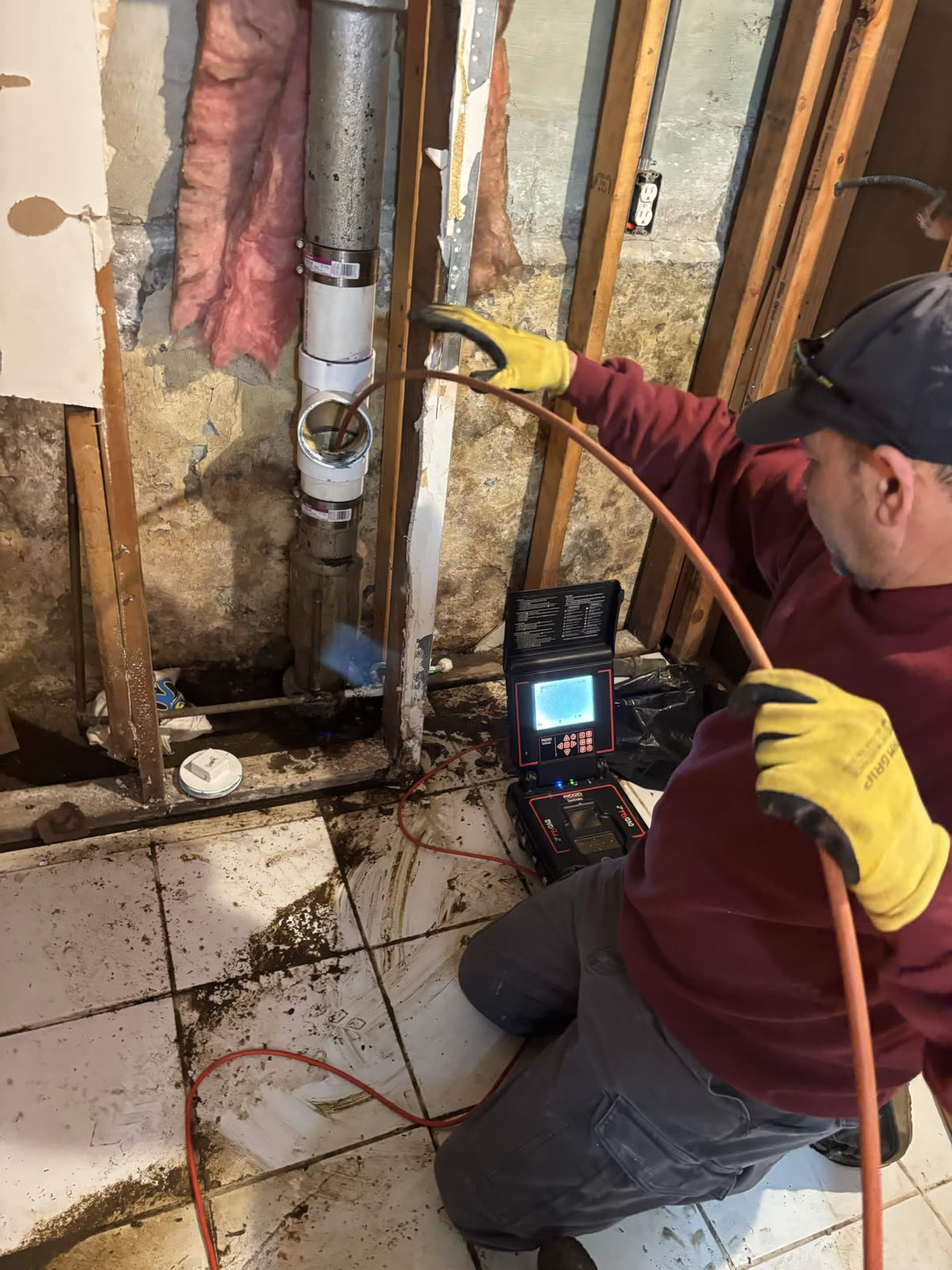 Plumber using a sewer camera inspection unit near a wall pipe